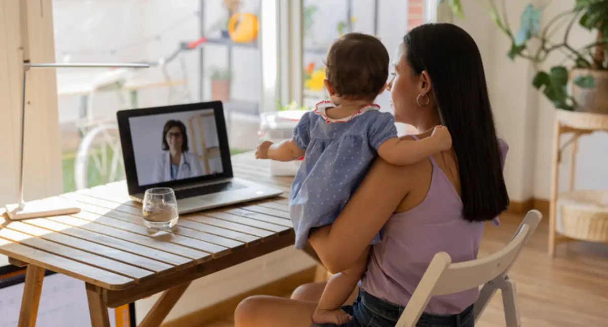 Une mère et son jeune enfant devant un écran d’ordinateur où apparait une médecin.